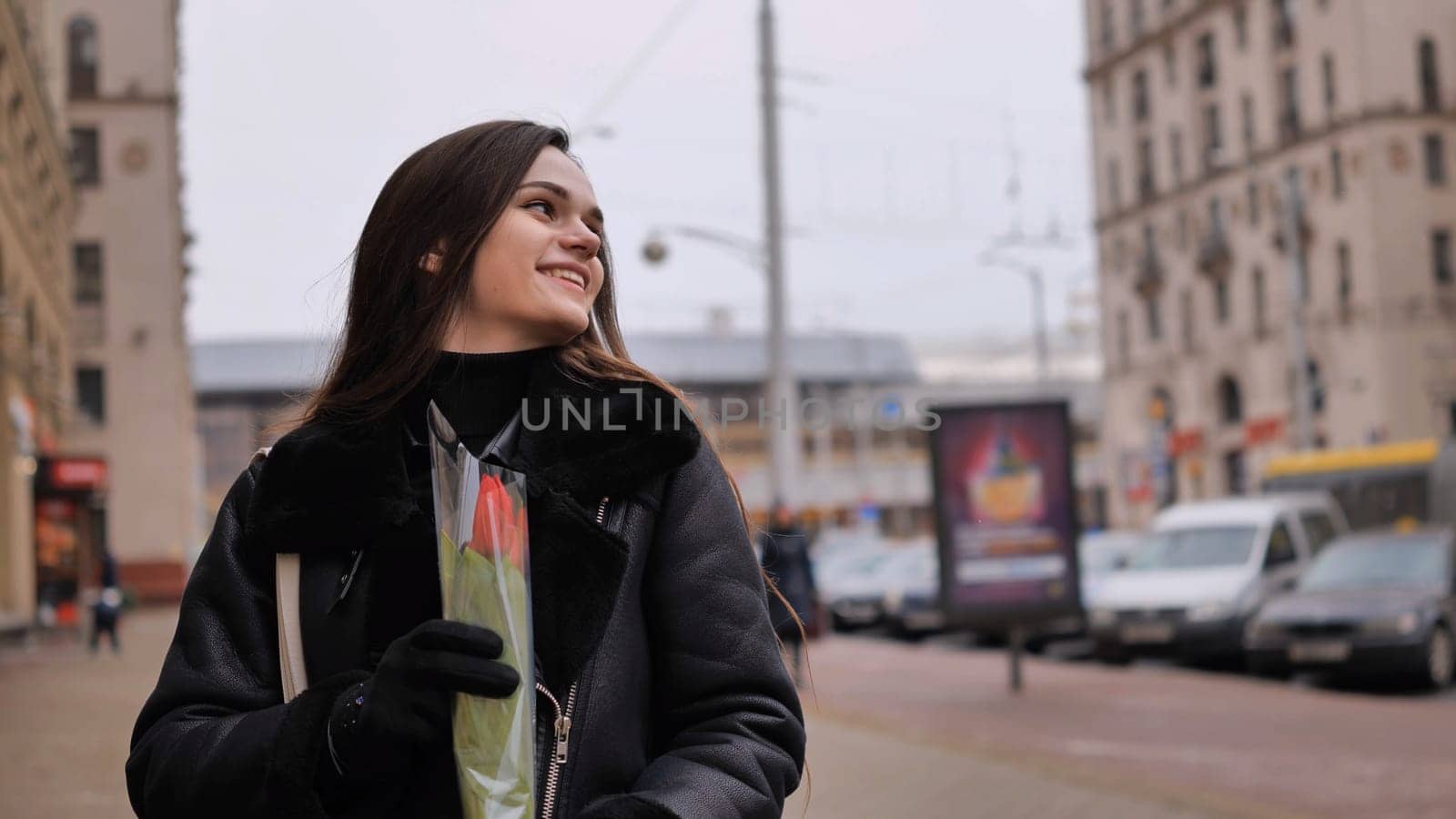 Portrait of a happy brunette girl with a tulip in the background of the city in the cold season