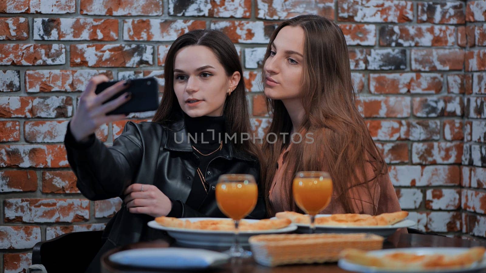 Two beautiful stylish young girls have lunch in a cafe and take a selfie by DovidPro