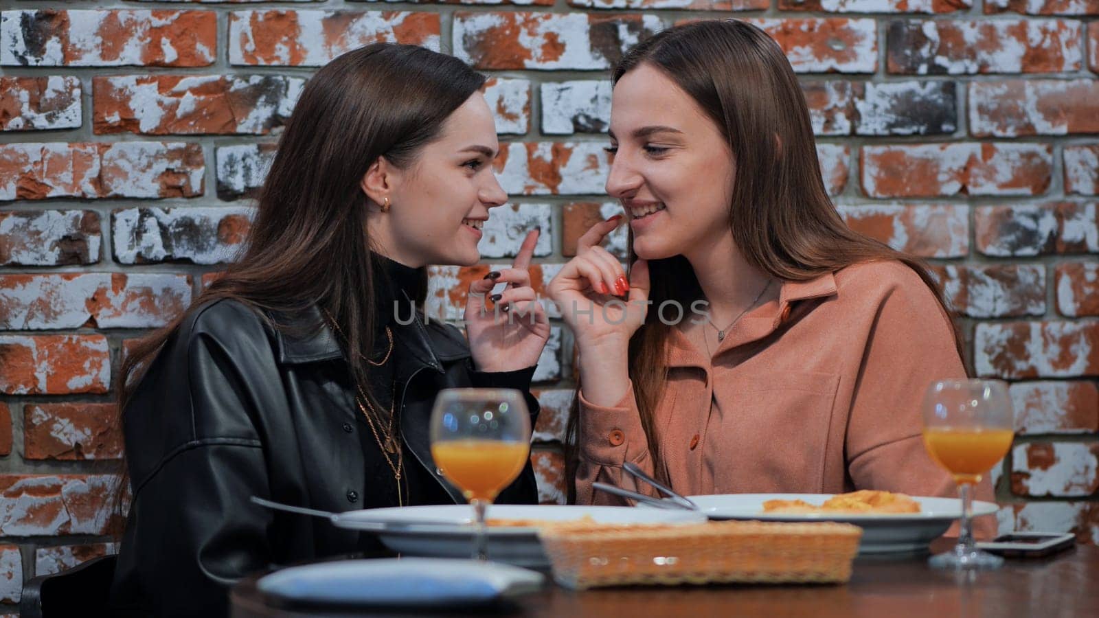 Two young girls gossiping sitting in a cafe. by DovidPro