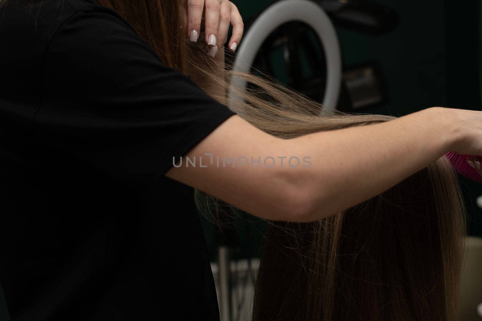 Beauty sphere. The master hairdresser does styling and combing the hair. Combs a client's long hair with a round brush and blow-dries it in a beauty salon. Close-up. Business concept. No faces.