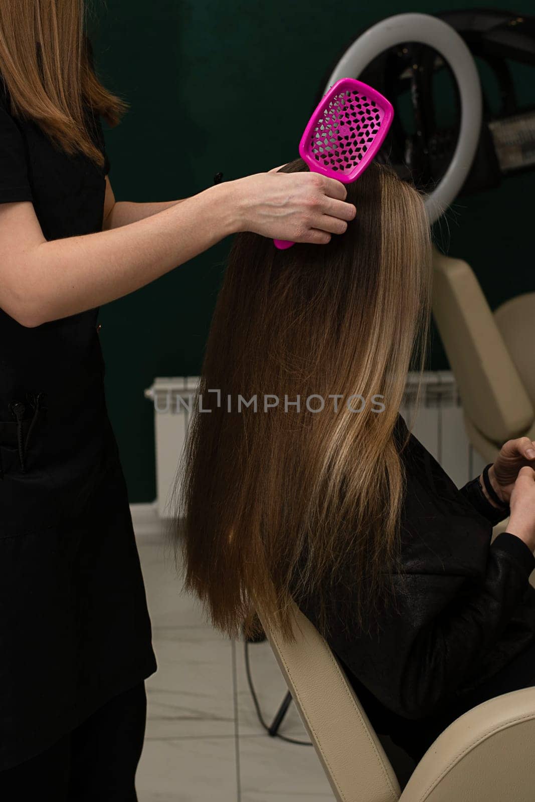 Beauty sphere. The master hairdresser does styling and combing the hair. Combs a client's long hair with a pink comb in a beauty salon. Close-up. Business concept. No faces. by ketlit