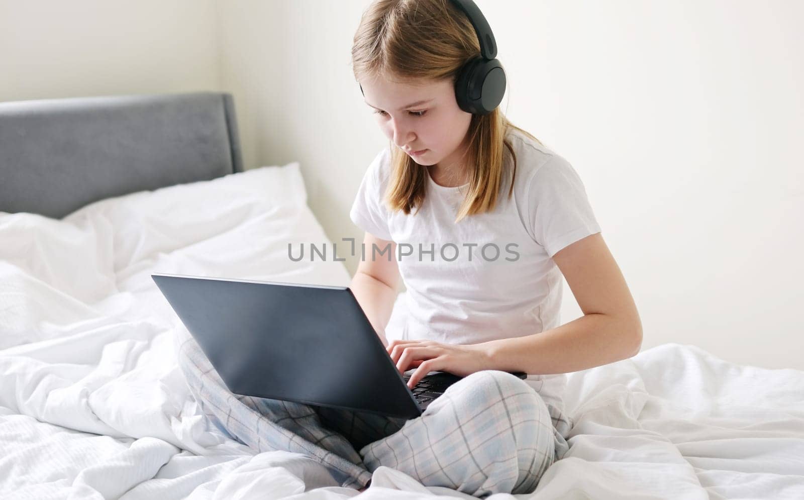 Focused Little Girl Doing Her Homework Online On A Large Bed In The Morning