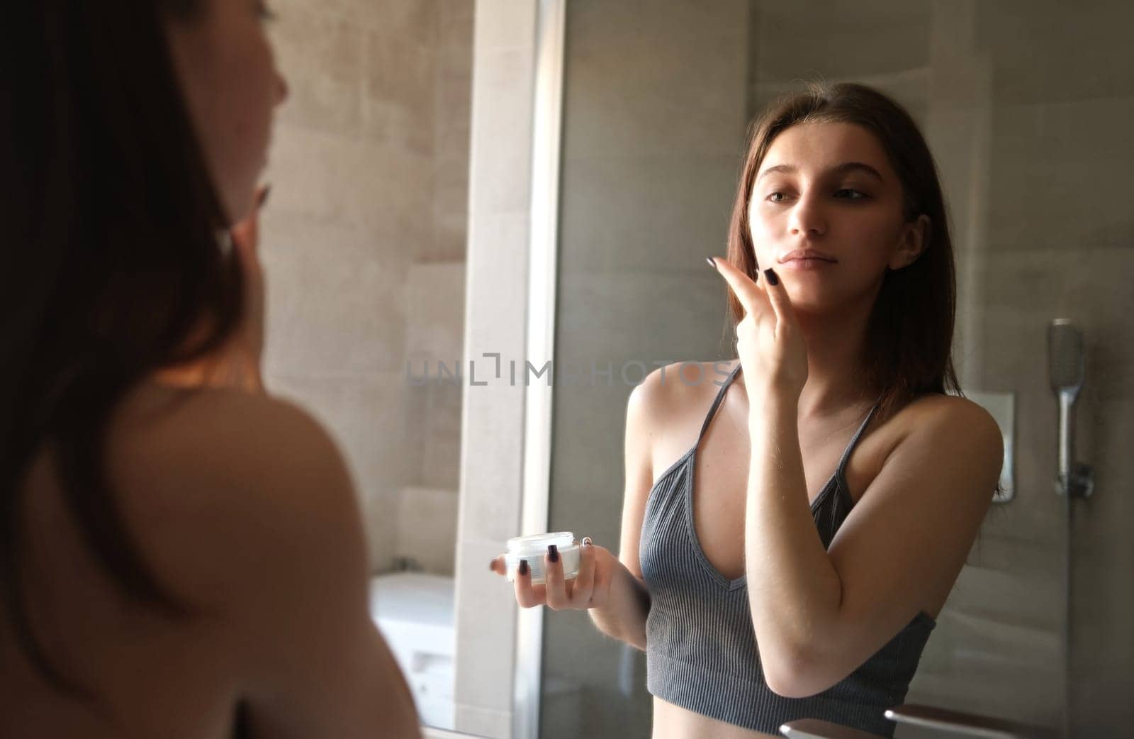 Young Girl Applying Cosmetic Skin Cream On Face And Body In Bath Mirror by GekaSkr