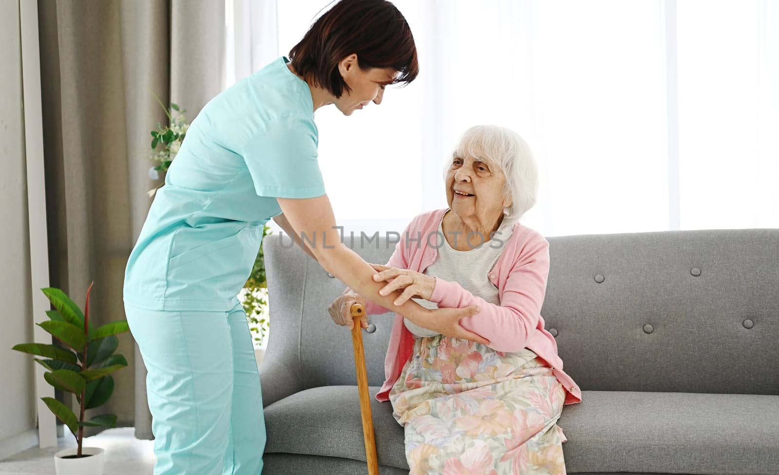 Nurse Hands Cane To Elderly Woman, Helping Her Move Around Room by GekaSkr