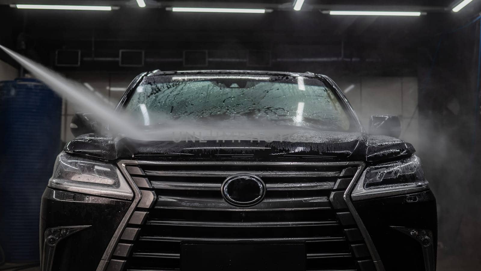 A man washes foam off a black car with water at a car wash