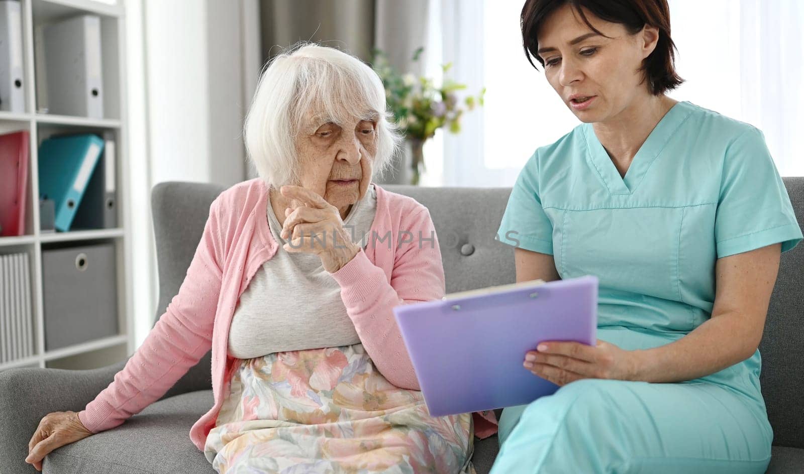 Doctor Records Old Woman'S Complaints On A Small Couch In A Large Bright Room