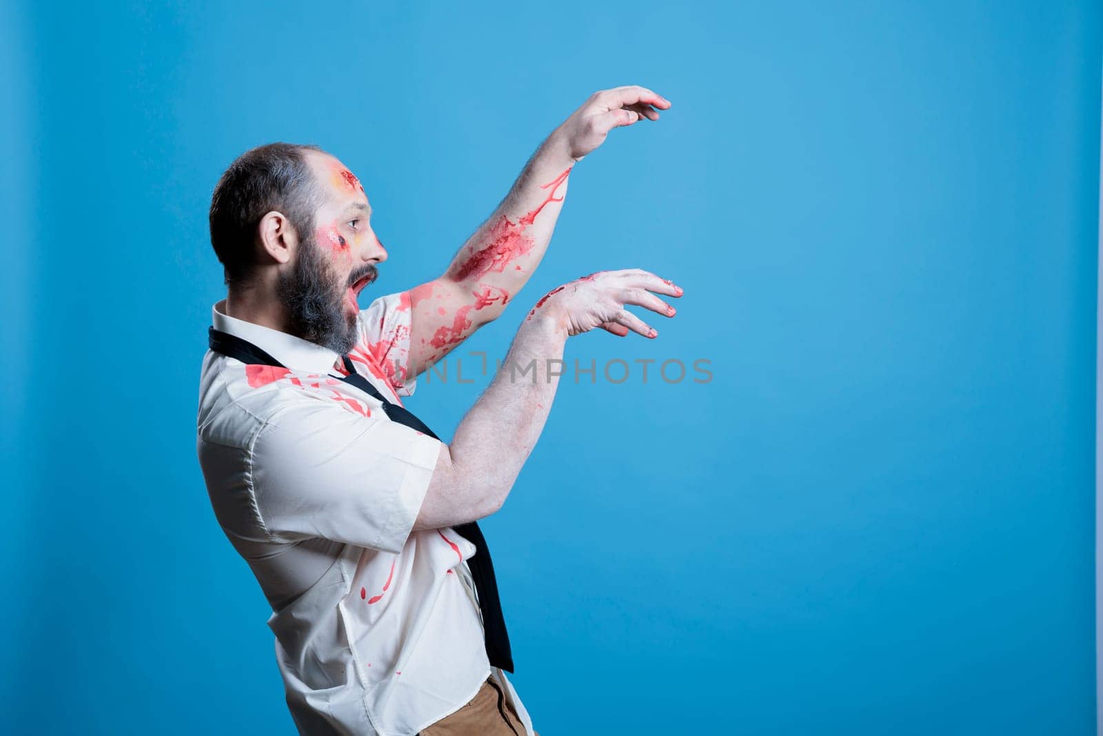 Possessed man covered in blood turned into zombie after being killed, haunting place. Wounded ghoulish cadaver limply walking towards victim, preparing for attack, studio background