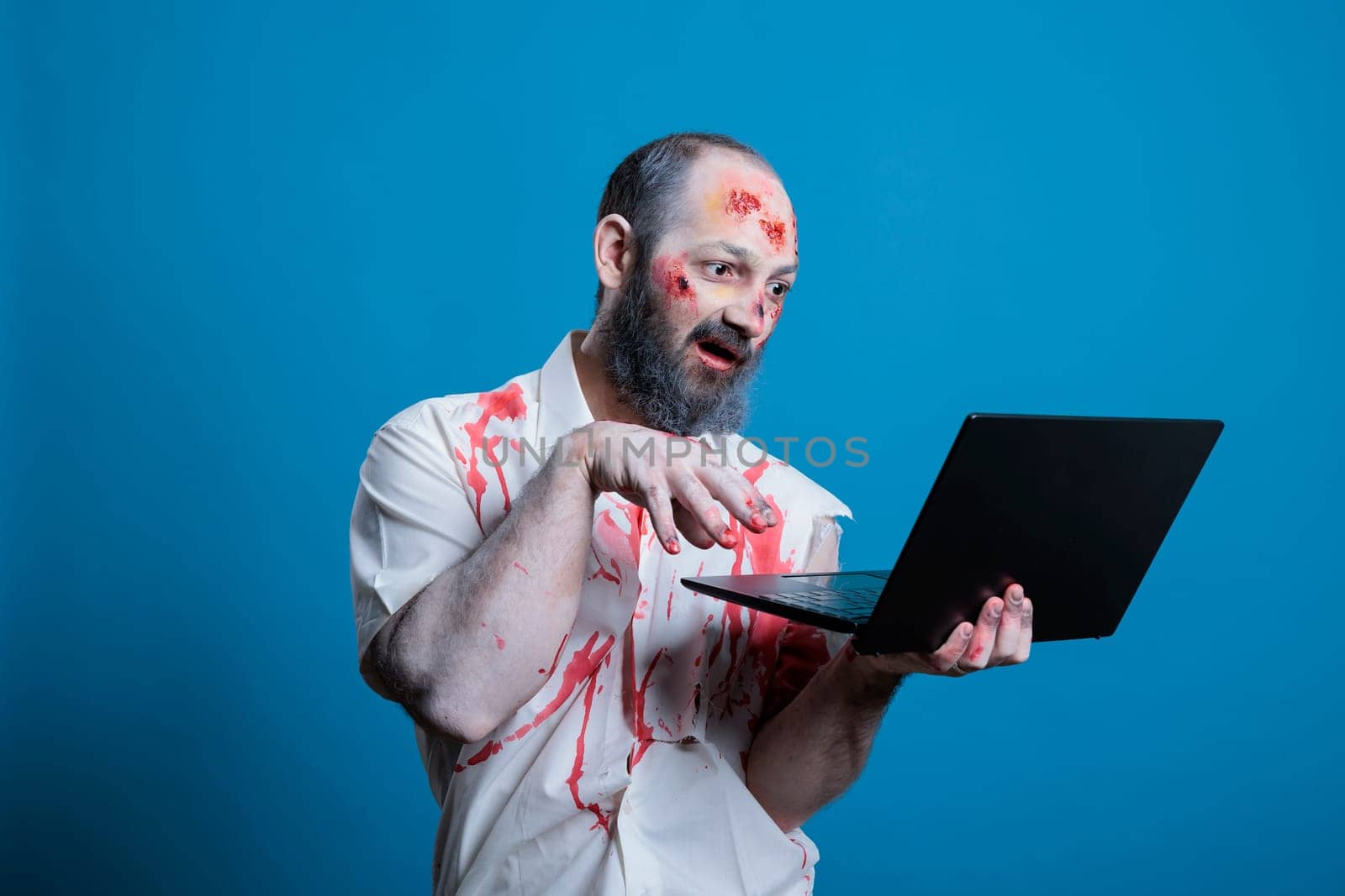Mindless businessman worked to death doing mind numbing tasks on laptop, suffering from burnout. Man working like zombie on notebook, trapped in capitalism rat race concept, studio background