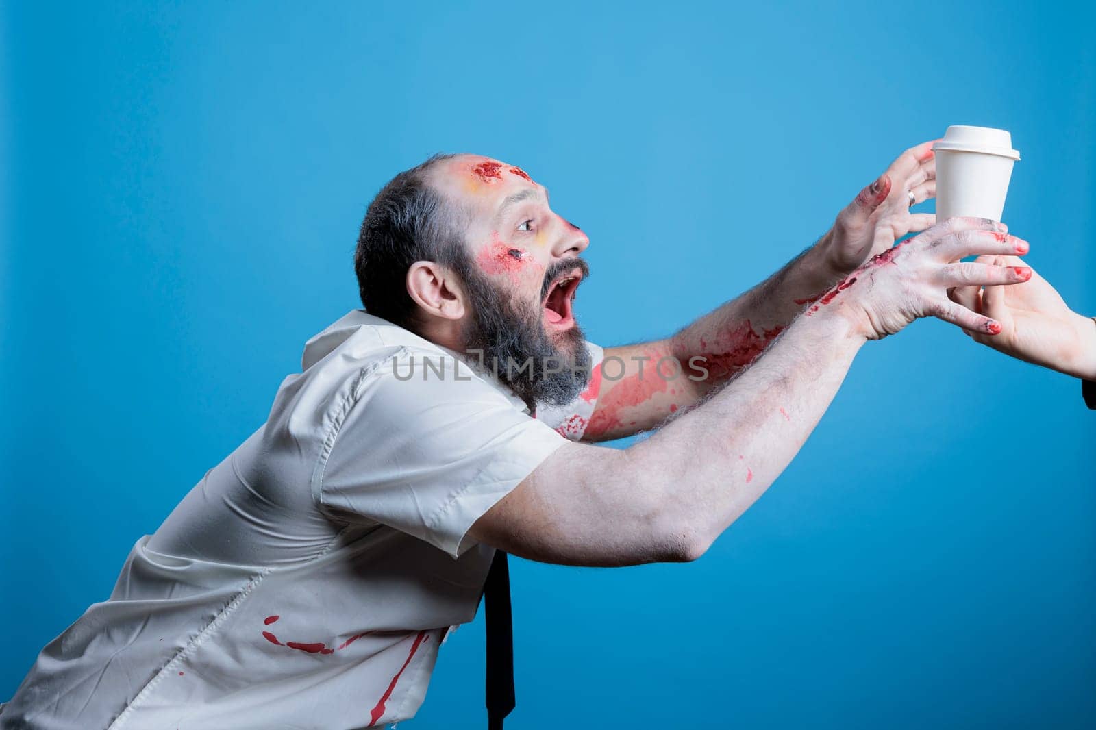 Thirsty sick junkie in need of coffee chasing it to get his fix and satisfy addiction. Businessman suffering from caffeine abuse addiction, looking like zombie without it, studio background