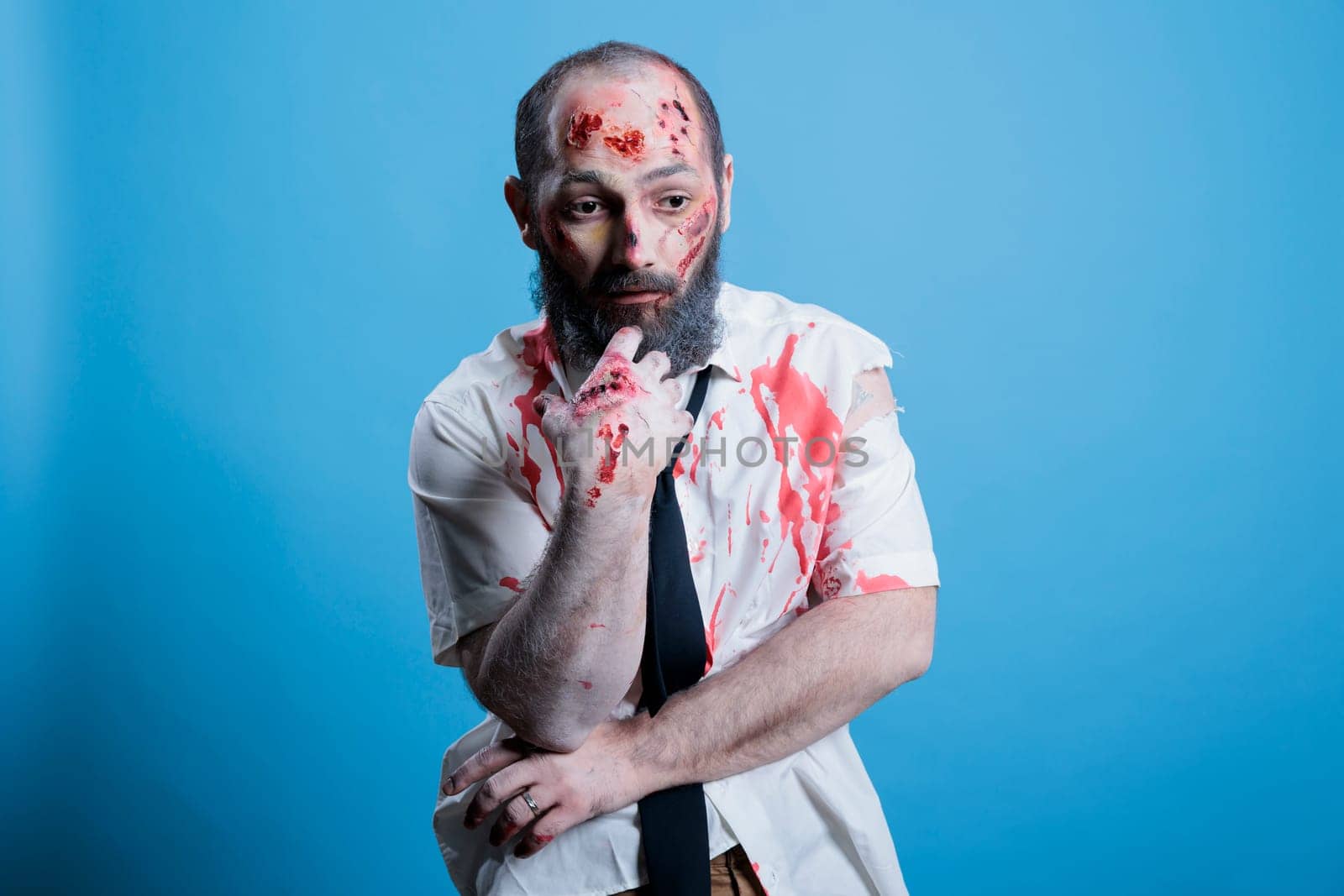 Actor dressed as horror movie brainless zombie repeating lines between scenes on set. Man costumed as mindless infected creature preparing for role, isolated over studio background