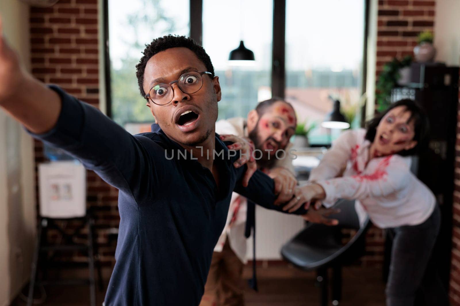 Close up of african american businessman grabbed by scary undead monsters in company office. Focus on apocalypse survivor pulled by brain eating zombies in blurry background