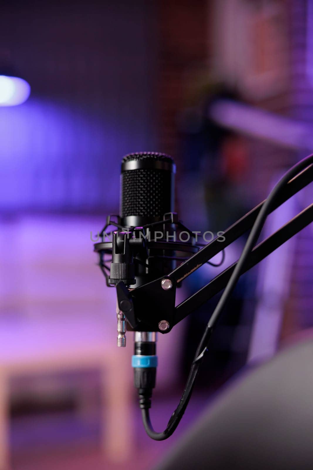 Close up shot of podcast microphone used to record conversations for internet livestreaming show. Streaming sound capturing and recording technology in empty home studio with neon lights