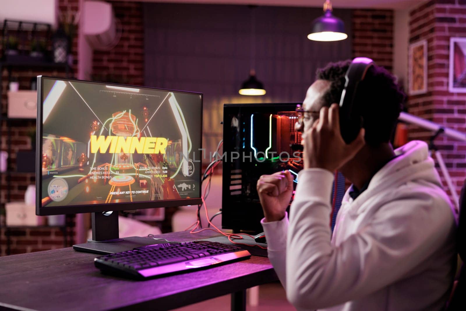 African american gamer excited about winning online multiplayer match against other players. Man seeing winner message on gaming PC computer display in neon lights living room