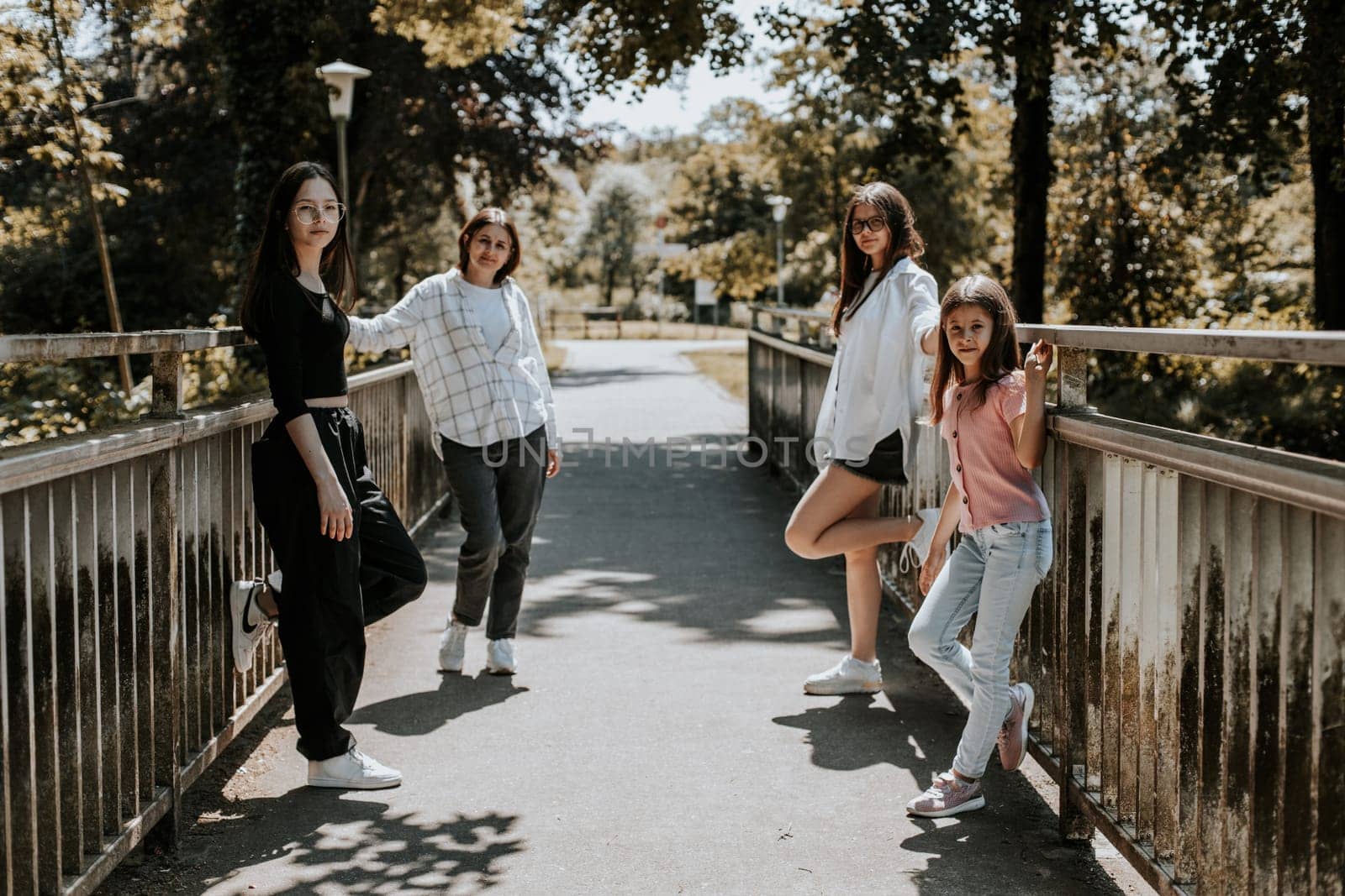Portrait of a young Caucasian mother with three grown daughters standing on an old wooden bridge in a city park on a summer day.