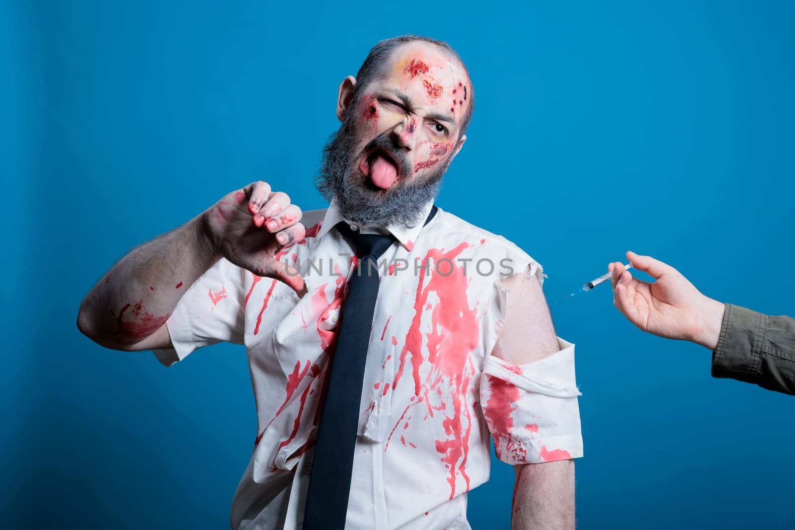 Man forced to take coronavirus vaccine shot showing thumbs down, conspiracy theory concept. Antivaxxer person receiving injection against will, showing disapproving hand gesture, studio background