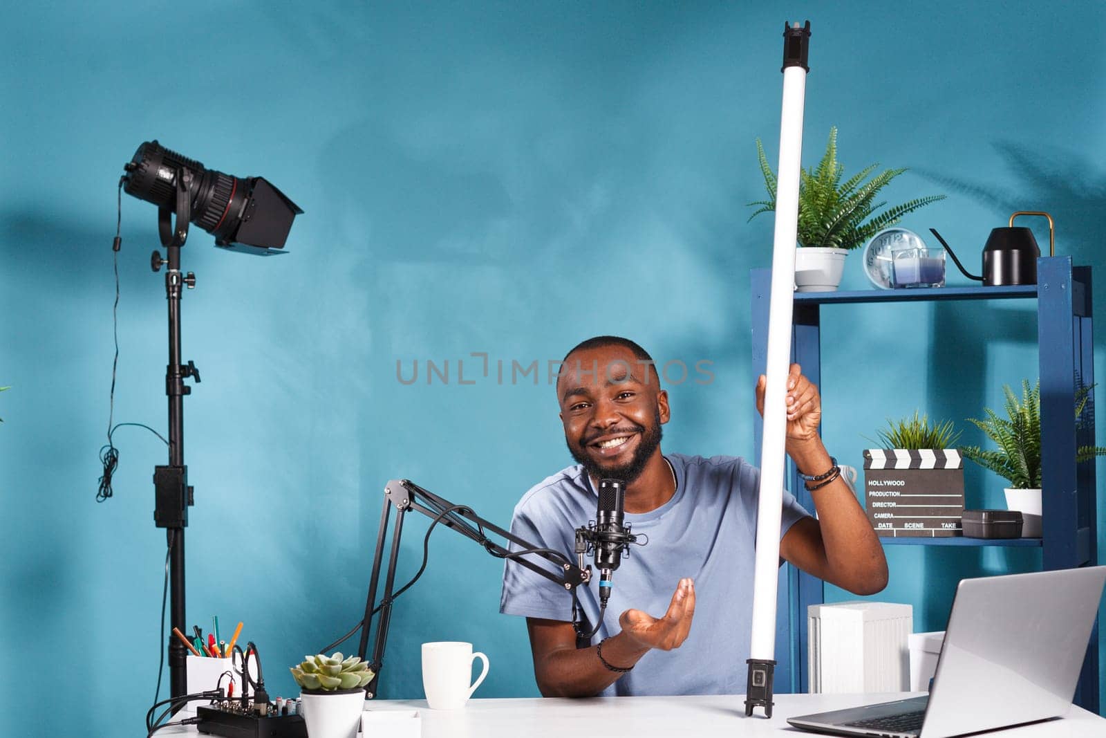 Smiling blogger holding tube light equipment and explaining features while recording video for online channel. Vlogger showing led lamp for photography studio and live streaming product review