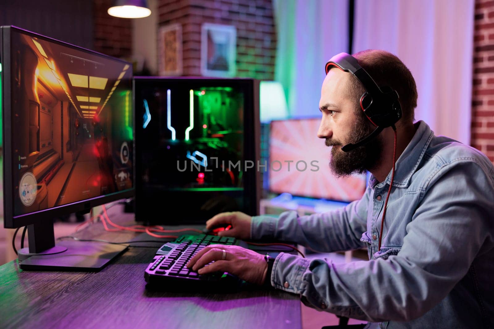 Pro gamer competing in intense online multiplayer videogame, streaming live from brick wall apartment. Focused man using gaming system and headphones for immersive experience