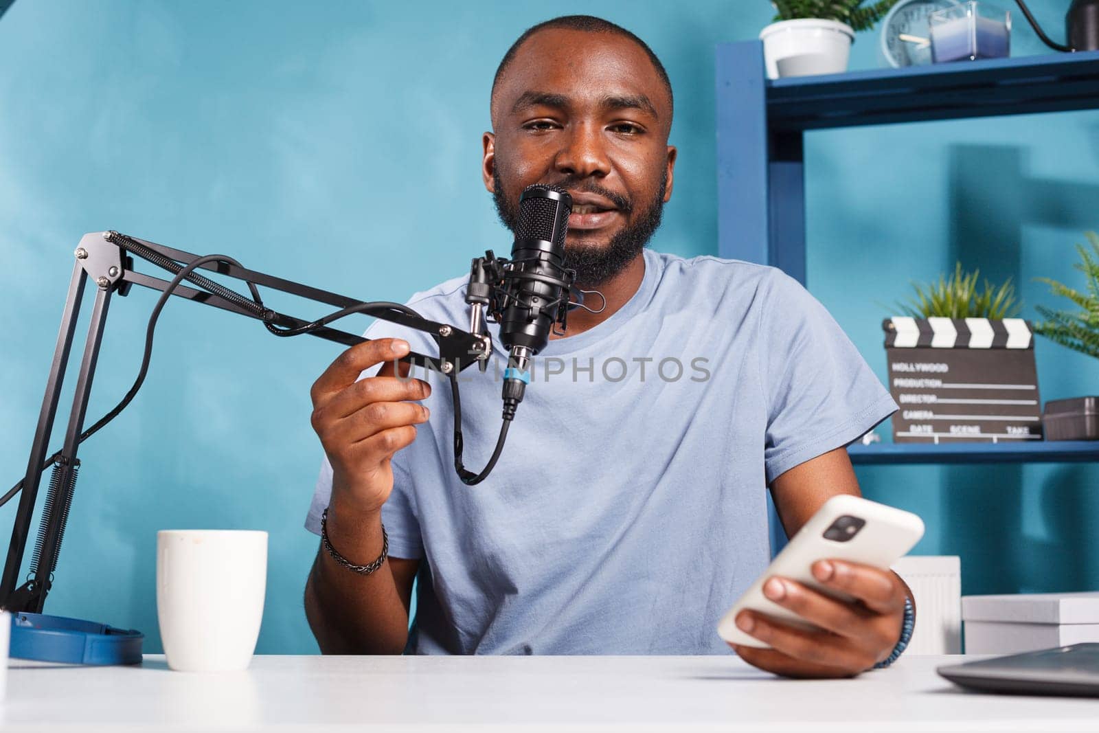 Vlogger creating podcast content while reading news from smartphone and looking at camera. African american man holding mobile phone and answering question while streaming live