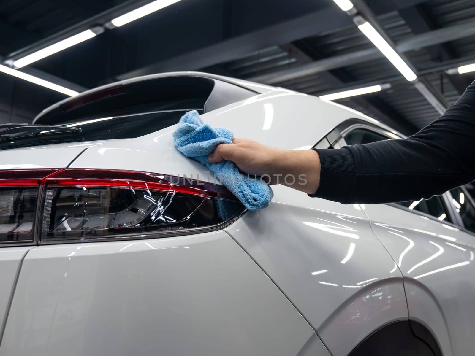 A mechanic wipes the body of a white car with a microfiber cloth. by mrwed54