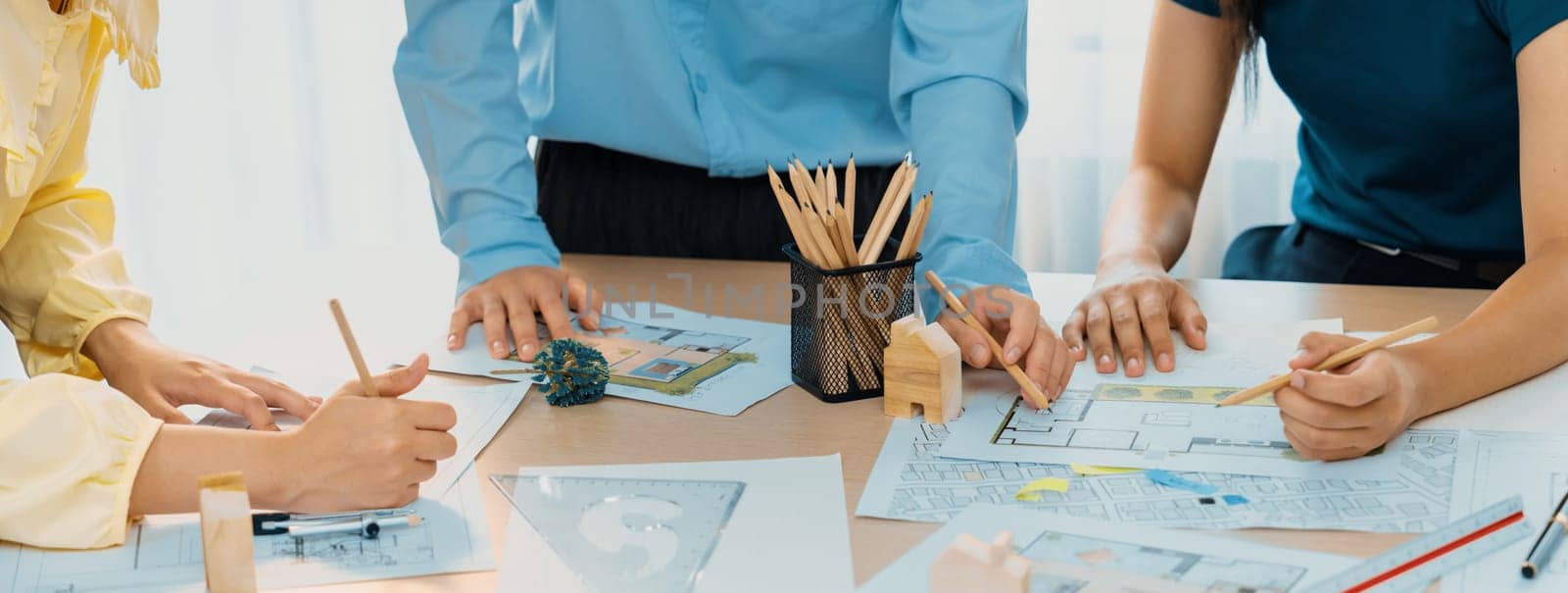 A portrait of professional architect team discussion about architectural project on meeting table with blueprint and wooden block scatter around at modern office. Closeup. Focus hand. Delineation.