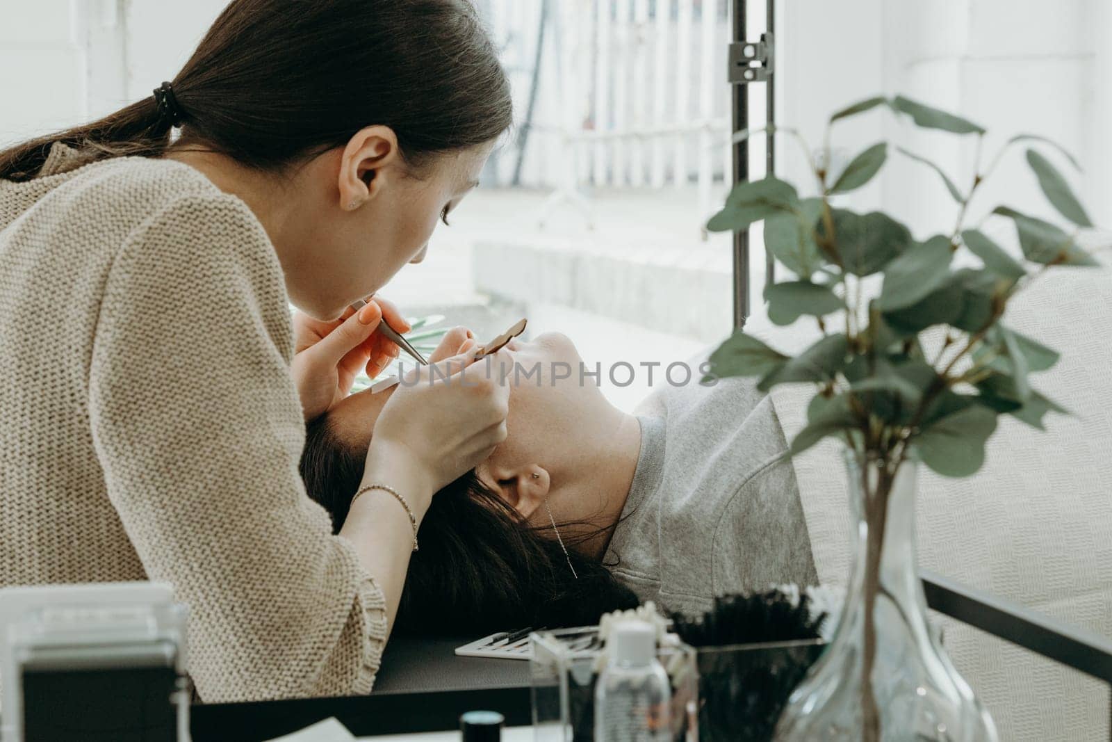A girl cosmetologist extends eyelashes to a woman. by Nataliya