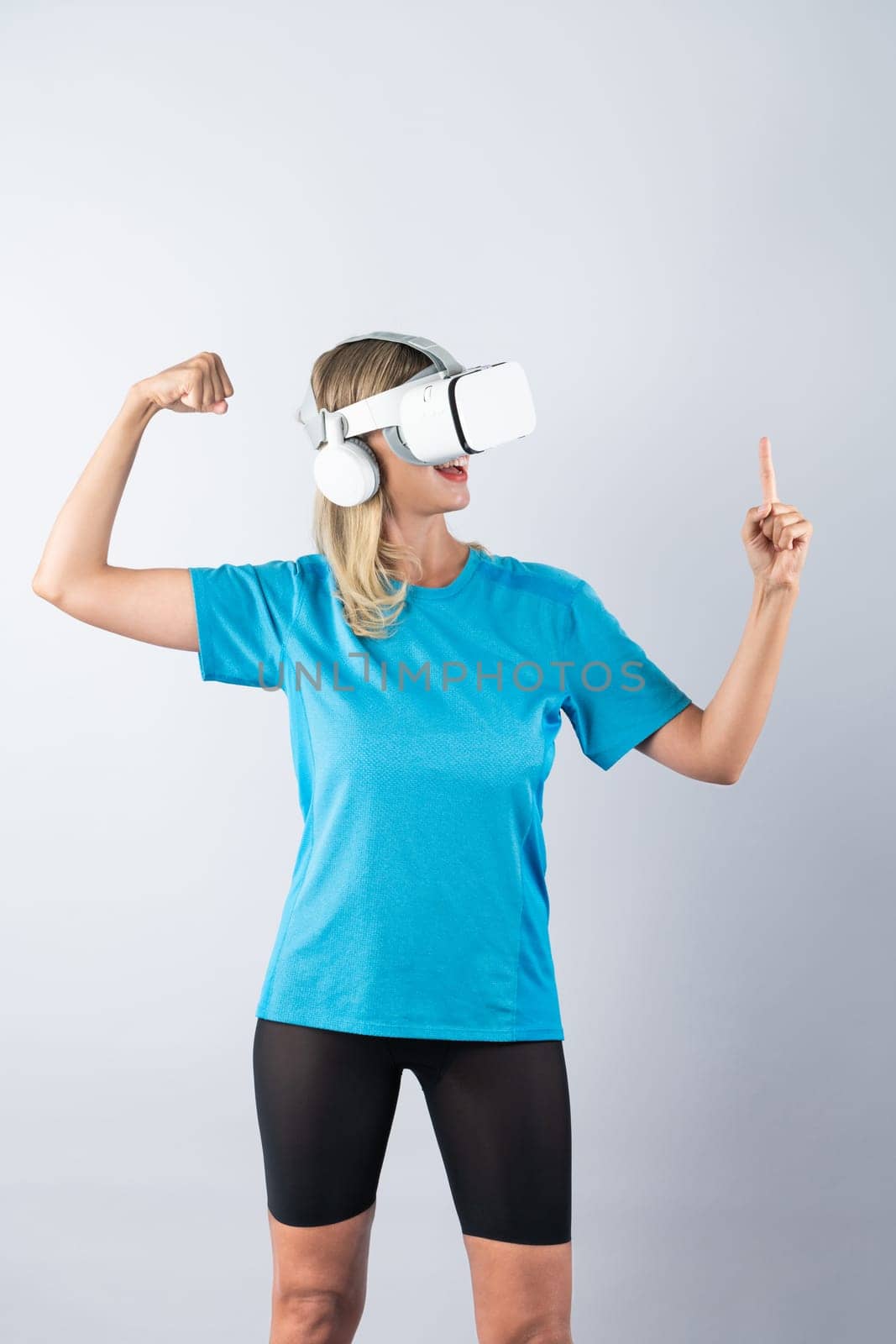 Girl pointing or spinning basketball while using VR glasses. Caucasian woman flexing while wearing casual shirt and visual reality goggles and standing at pink background. Innovation. Contraption.