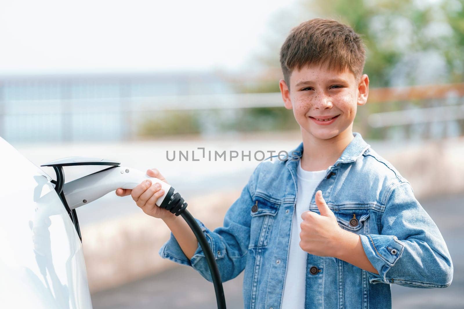 Little boy recharging eco-friendly electric car from EV charging station. EV car road trip travel by the seashore by alternative vehicle powered by clean renewable and sustainable energy. Perpetual