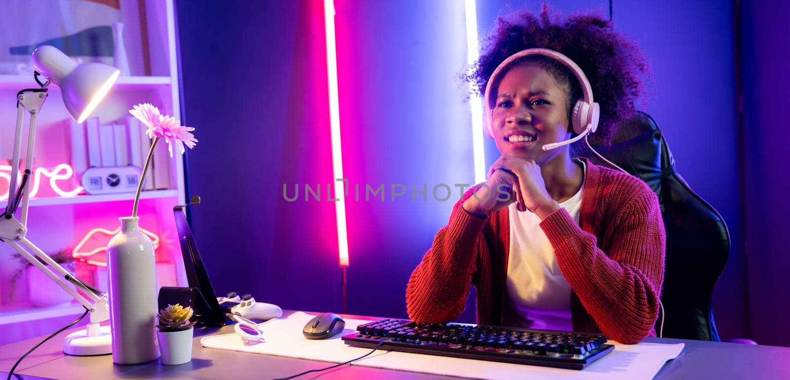 African American girl streamer playing online fighting with Esport skilled team wearing headphones in neon color lighting room. Talking other players planing strategies to win competitors. Tastemaker.