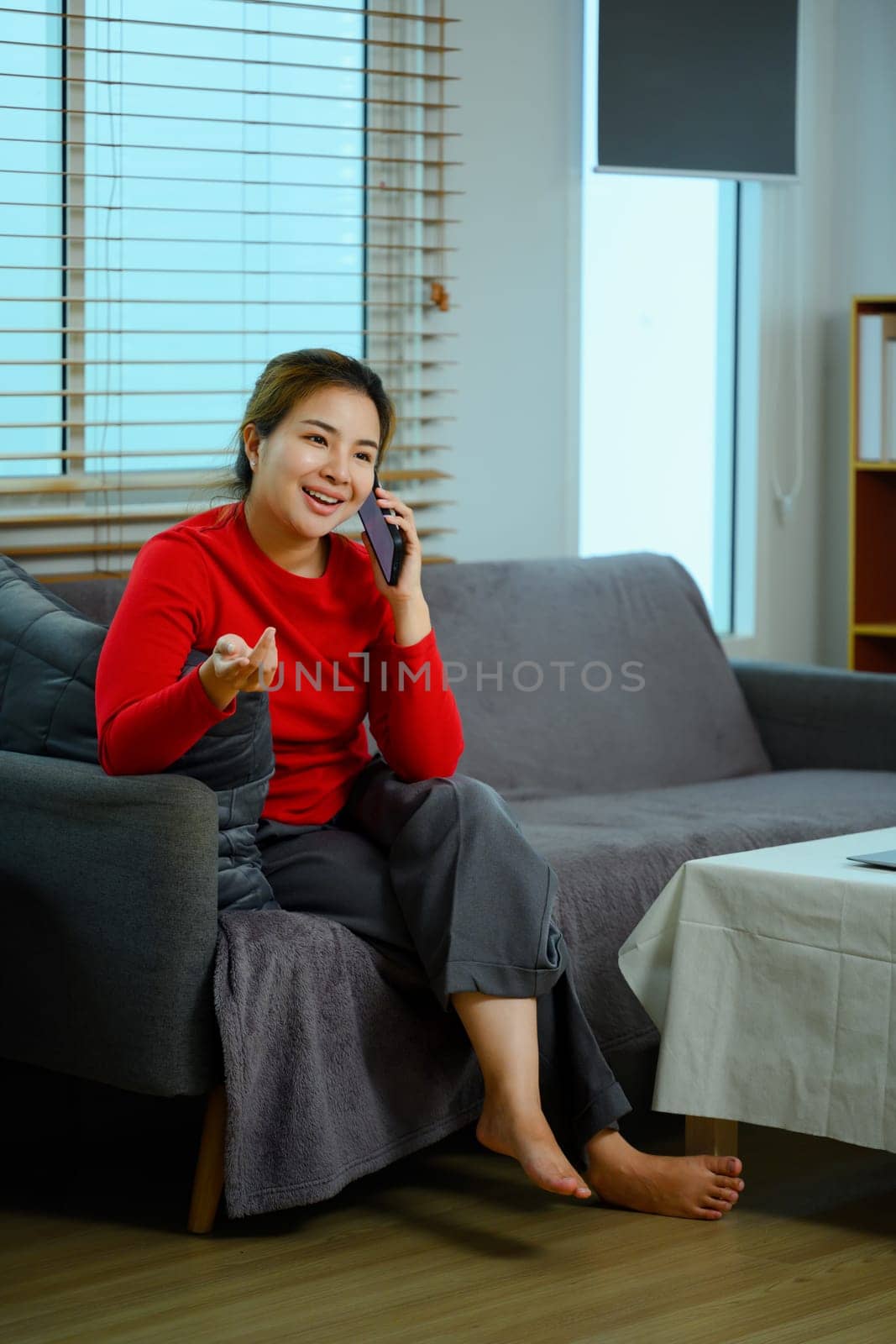 Cheerful young woman having phone conversation sitting on sofa at home.