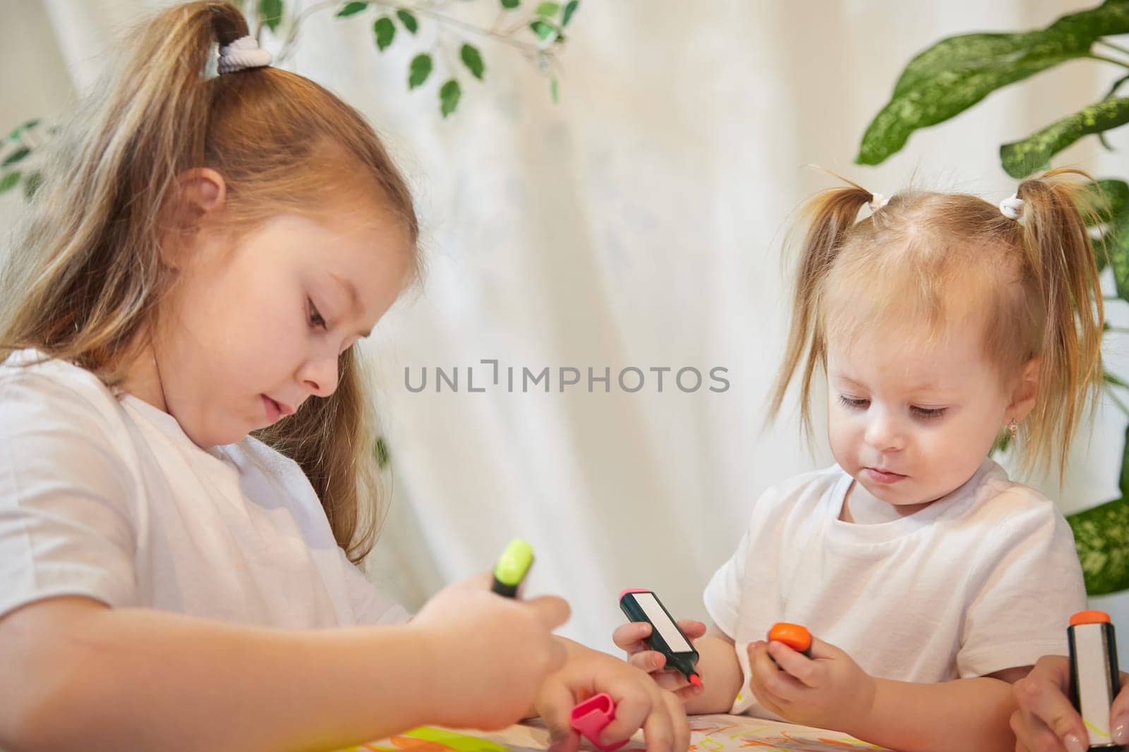 Cute little sisters are painting on table. Preschooler, 4 and 8 years child in living room. Small girl kids doing homework, home schooling concept