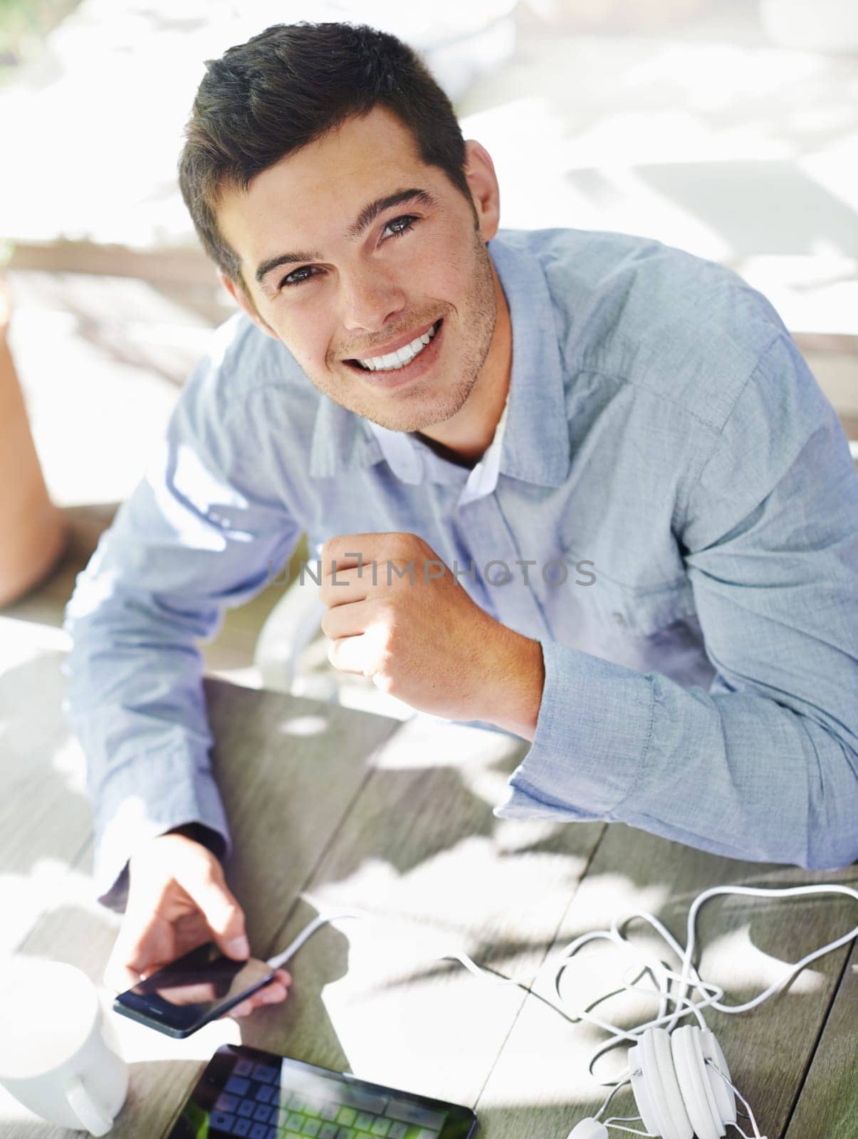 Smile, table and portrait of man with phone for online networking, communication and social media. Happy, male person and high angle with technology in garden for website, streaming and information.