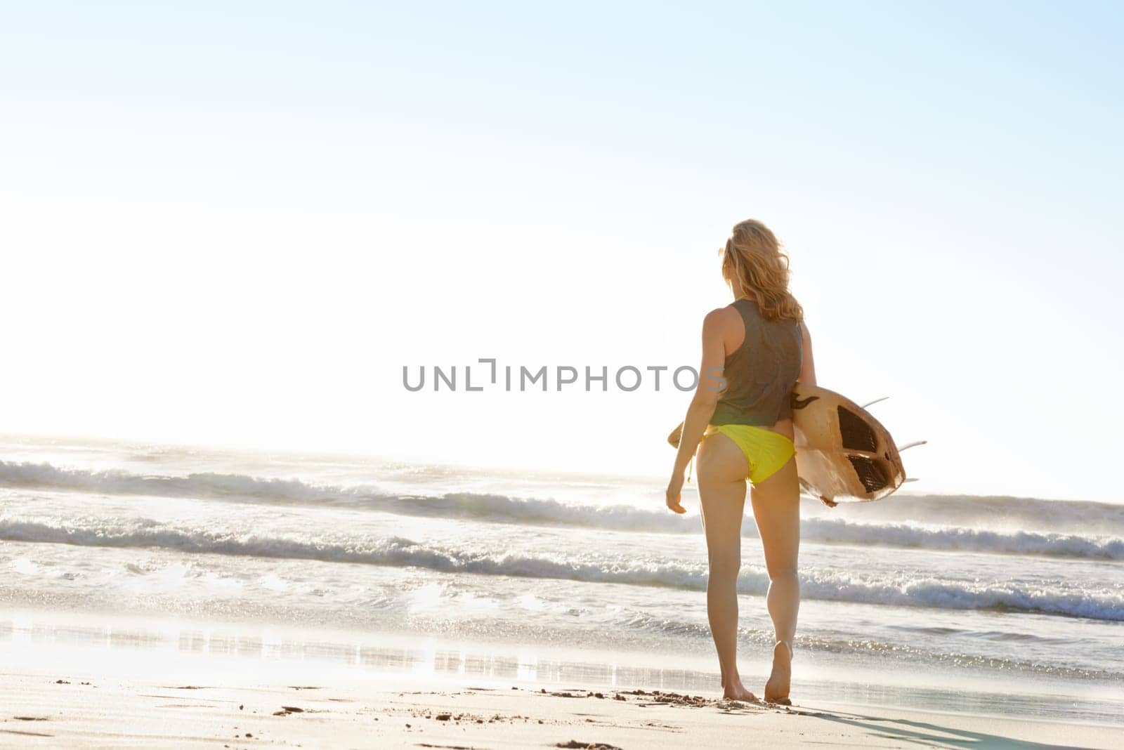 Woman, surfer and beach with surfboard, waves or blue sky for sport, hobby or outdoor freedom. Rear view of active female person in bikini on sand or ocean coast for swim or surfing with mockup space by YuriArcurs