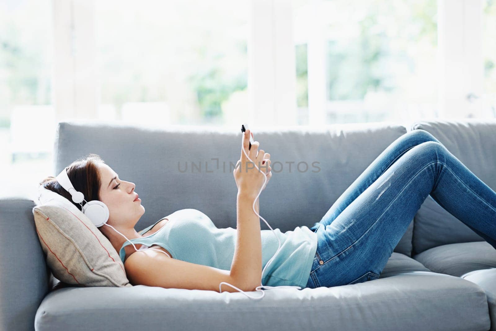 Girl, headphones and phone on sofa in house for music, relax and self care while on study break. Woman, headset and smartphone on couch in home living room for social media, video and app or radio by YuriArcurs