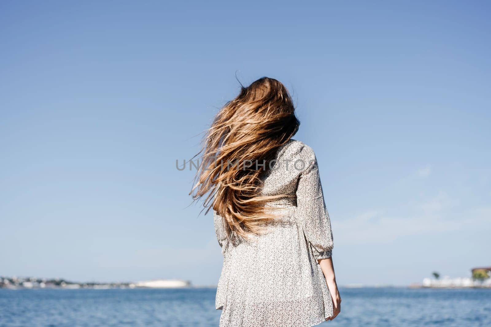 woman with long hair stands in front of a blue sky. She is wearing a white and black striped shirt. by Matiunina