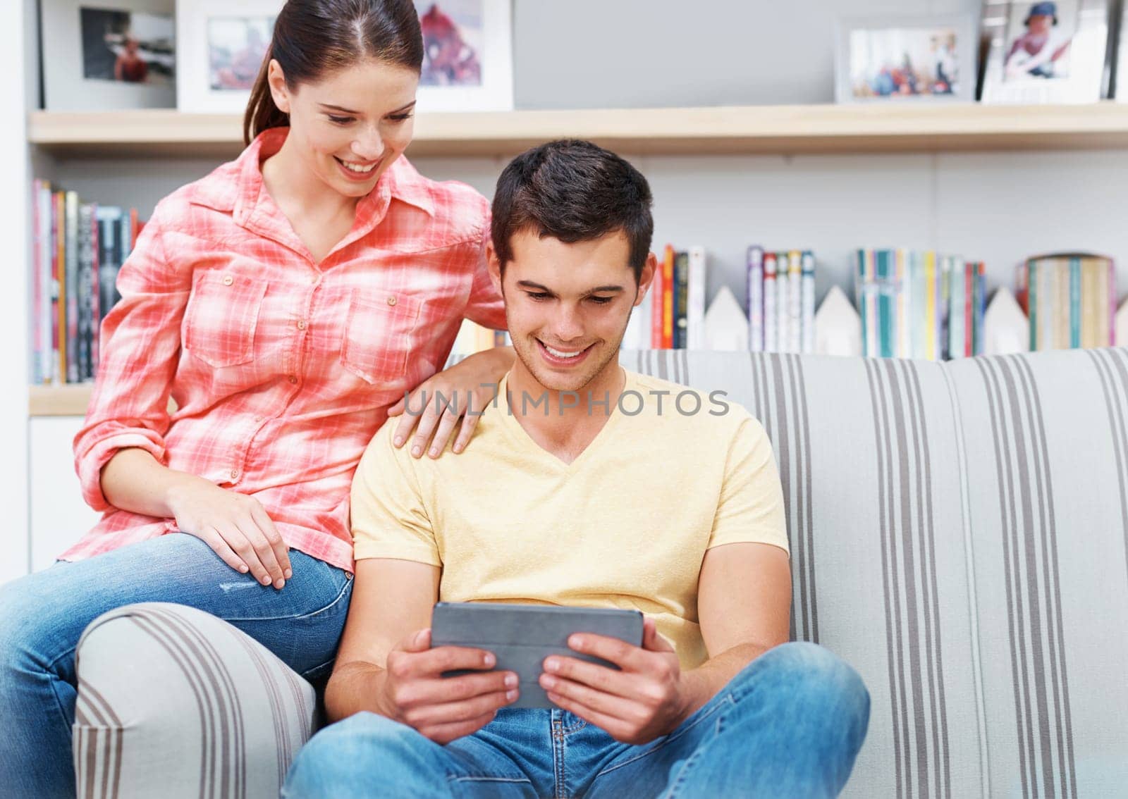 Couple, home and smile with tablet on sofa for social media, networking and entertainment. People, couch and living room on internet or online with streaming platform for videos, fun and memes by YuriArcurs