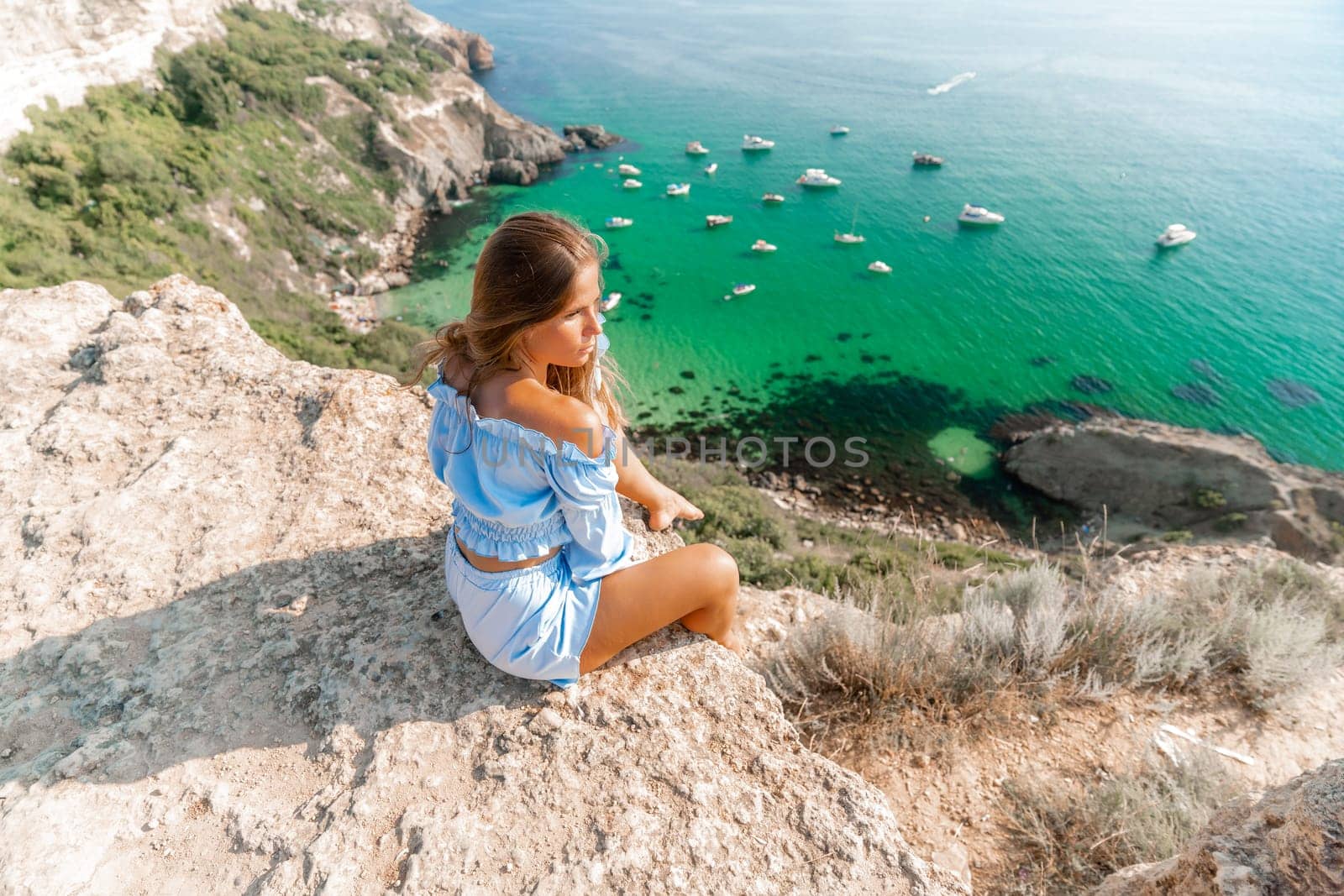 Woman travel sea. Happy woman in a beautiful location poses on a cliff high above the sea, with emerald waters and yachts in the background, while sharing her travel experiences by Matiunina