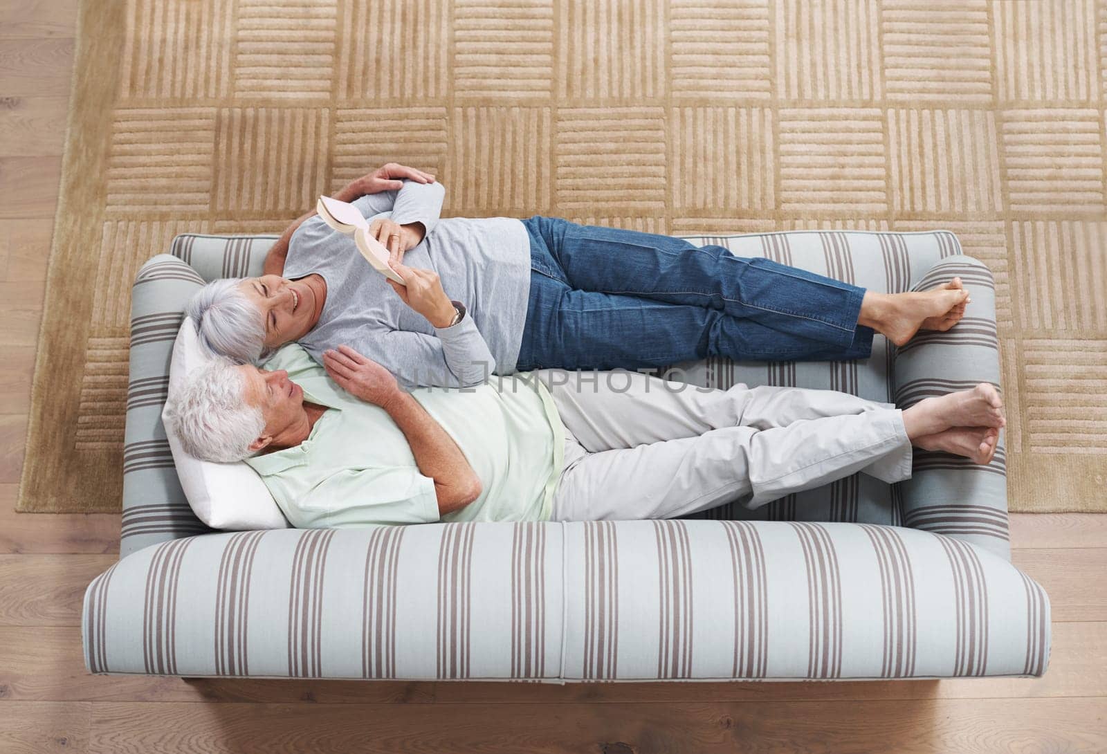 Top view, senior couple and reading book on sofa in living room for story, knowledge and relax in home. Retirement, elderly man and woman lying on couch for love, information and bonding together.