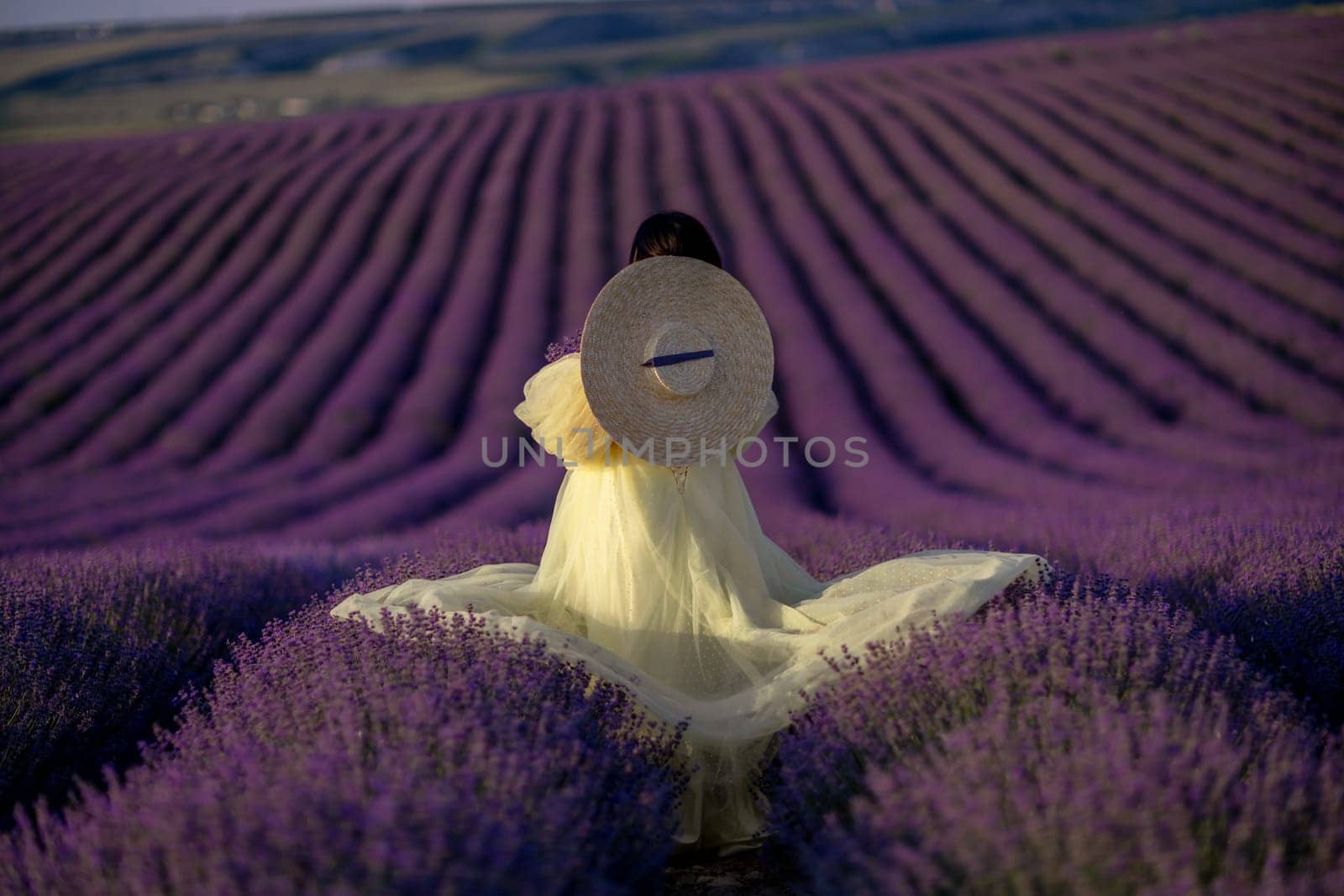 Woman lavender field sunset. Back view woman in yellow dress and hat. Aromatherapy concept, lavender oil, photo session in lavender.