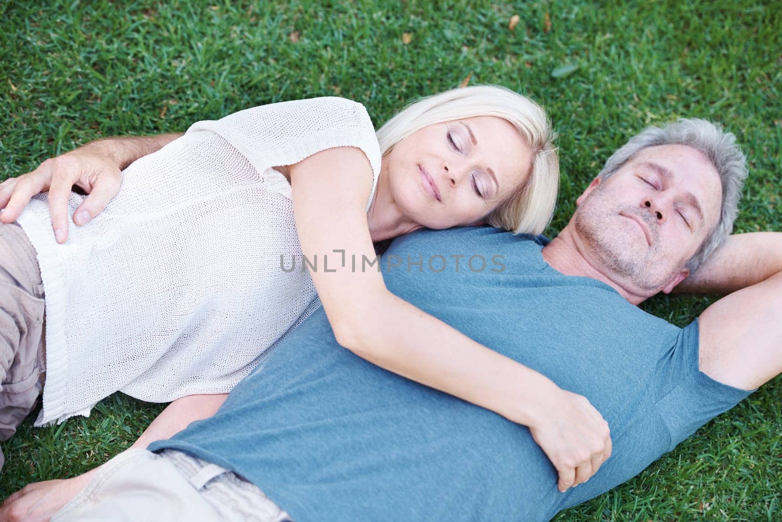 Man, woman and mature or relax on grass for afternoon nap in nature backyard for resting, weekend or sleeping. Couple, embrace and bonding connection with peaceful calm in Australia, meadow or spring by YuriArcurs