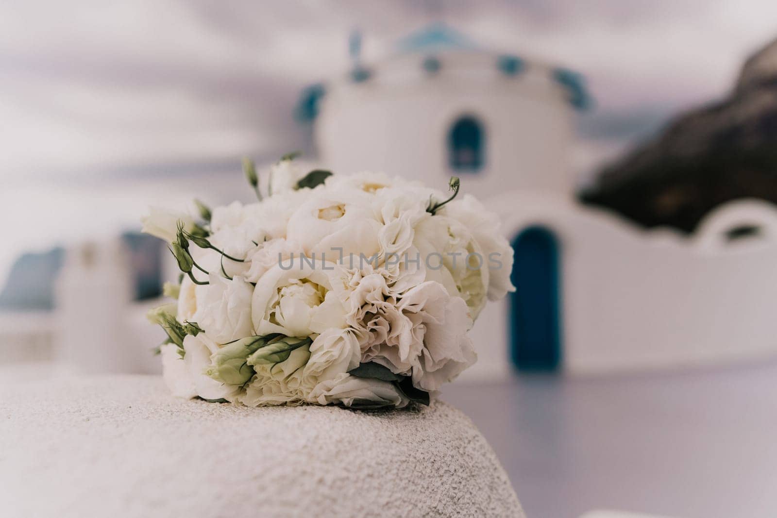 A bouquet of white flowers sits on a ledge next to a blue building. The flowers are arranged in a vase and are the main focus of the image. The blue building in the background adds a sense of calm