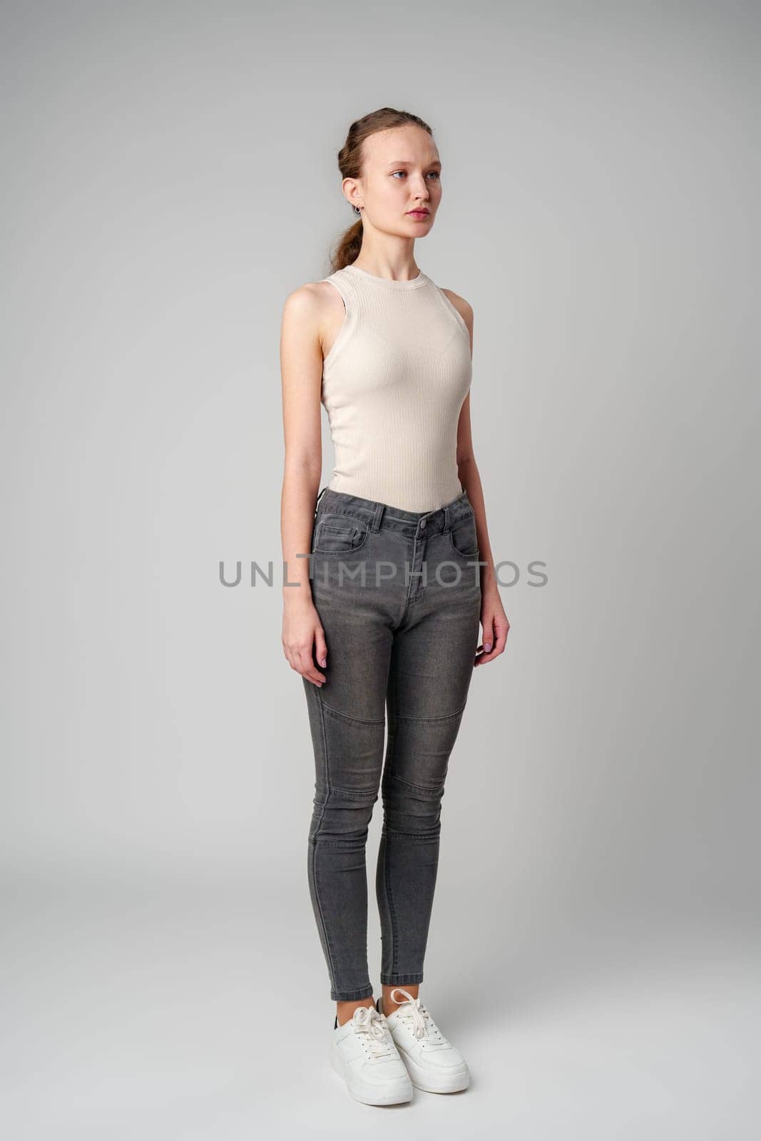 Girl in Beige Tank Top and Grey Jeans on gray background in studio