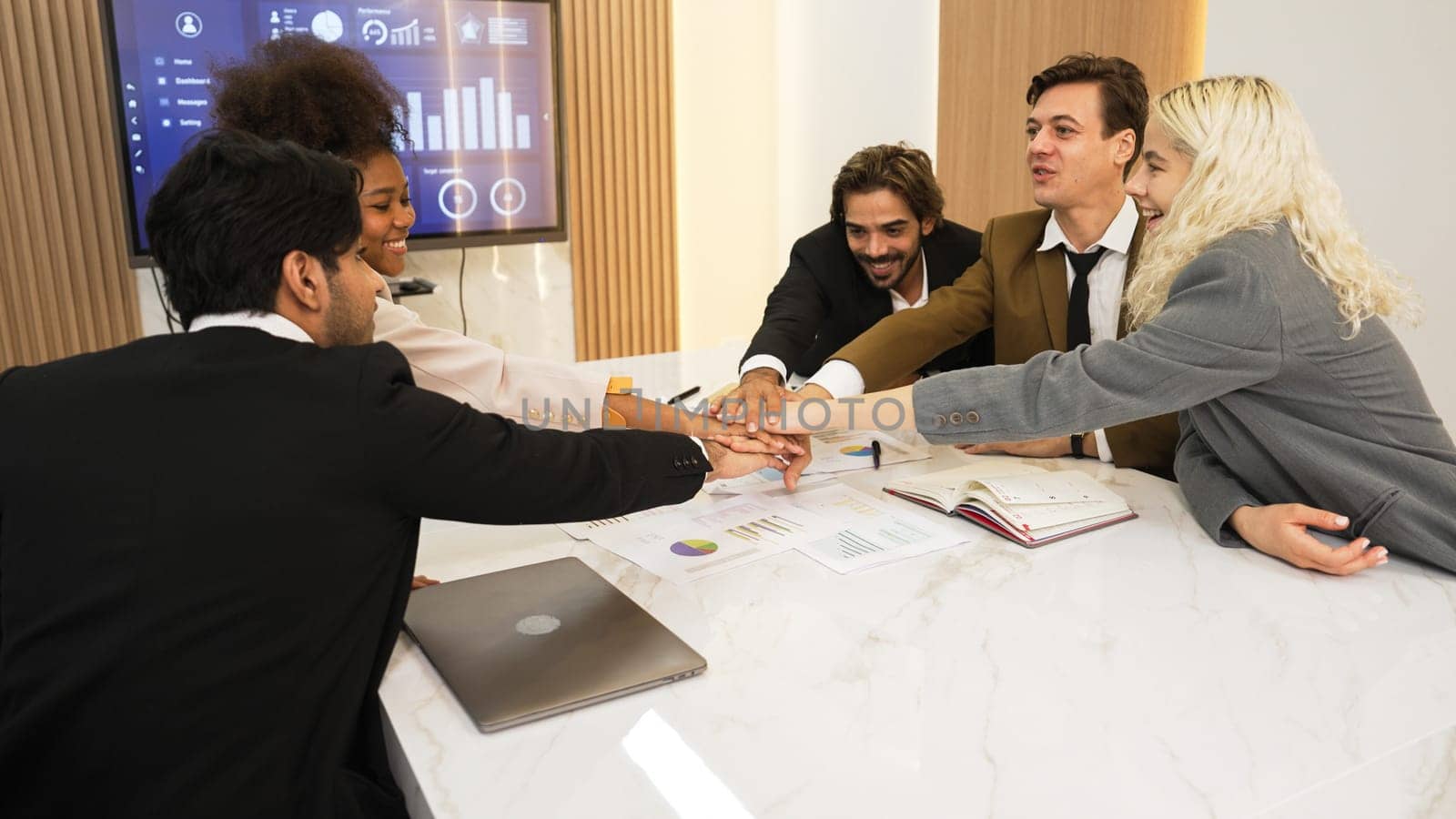 Group of diverse office worker join hand together in ornamented office room symbolize business synergy and strong productive teamwork in workplace. Cooperation and unity between business employee.