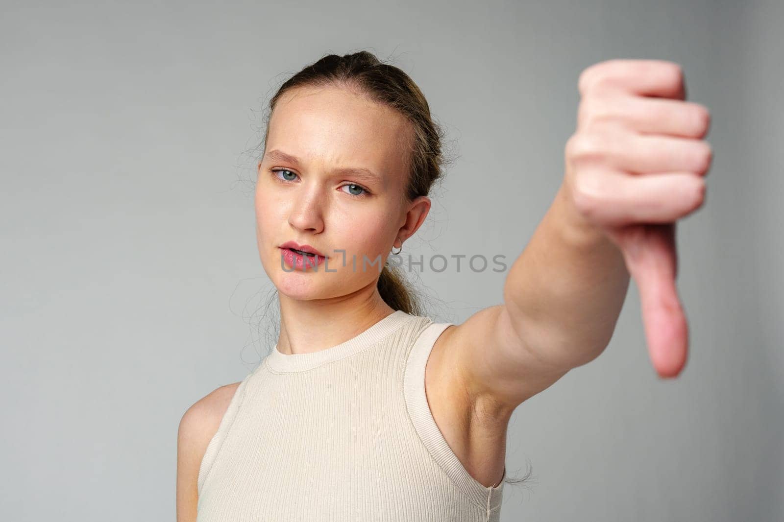 Young Woman Giving Thumbs Down Gesture Against a Neutral Background. by Fabrikasimf