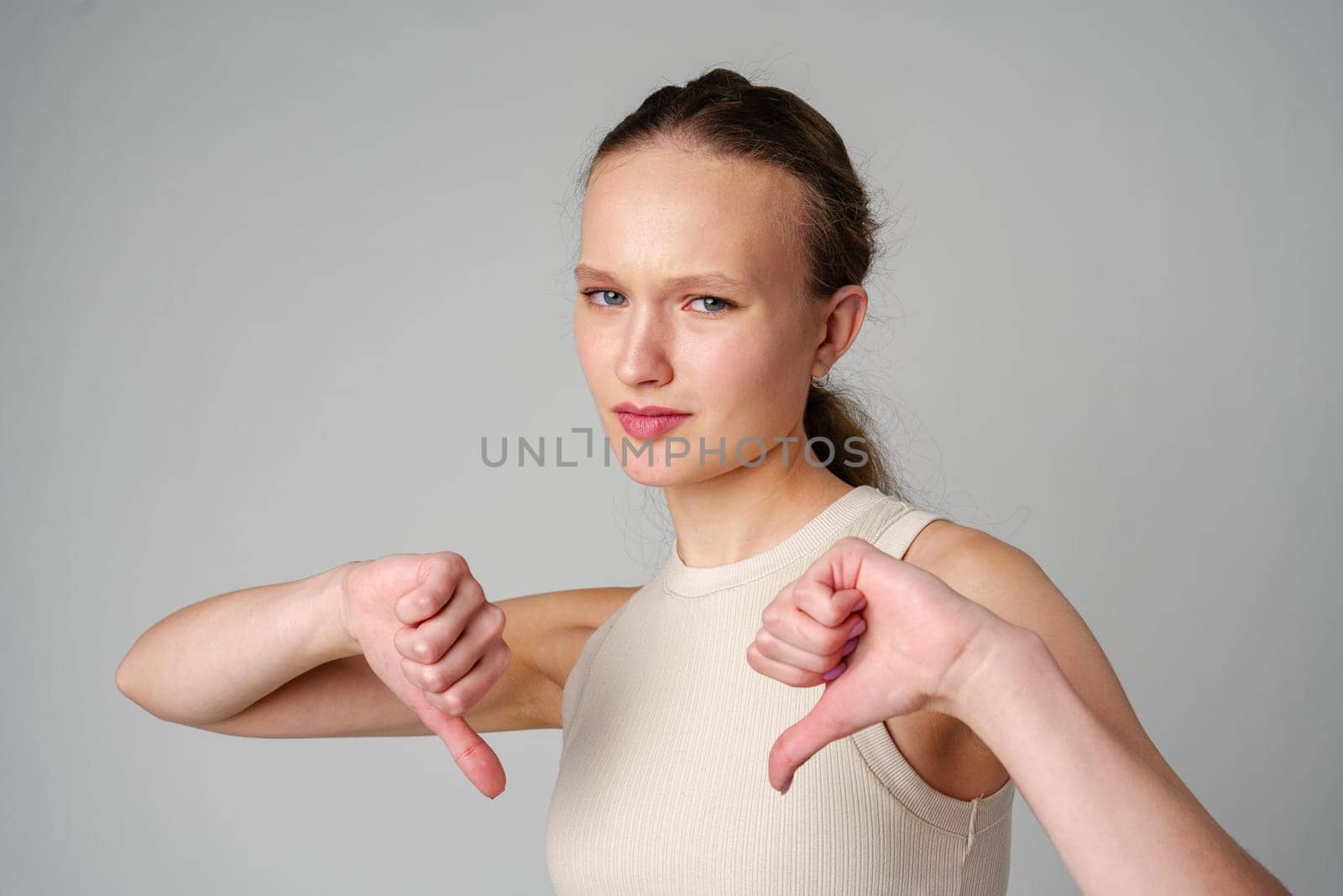 Young Woman Giving Thumbs Down Gesture Against a Neutral Background. by Fabrikasimf