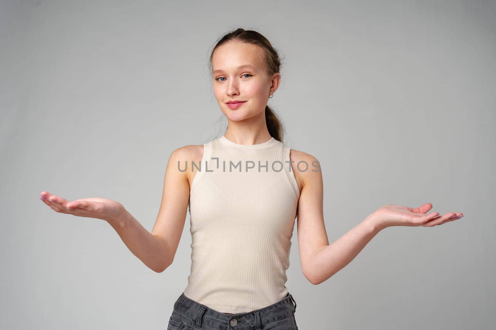 Young Clueless Woman Standing With Outstretched Arms on gray background in studio