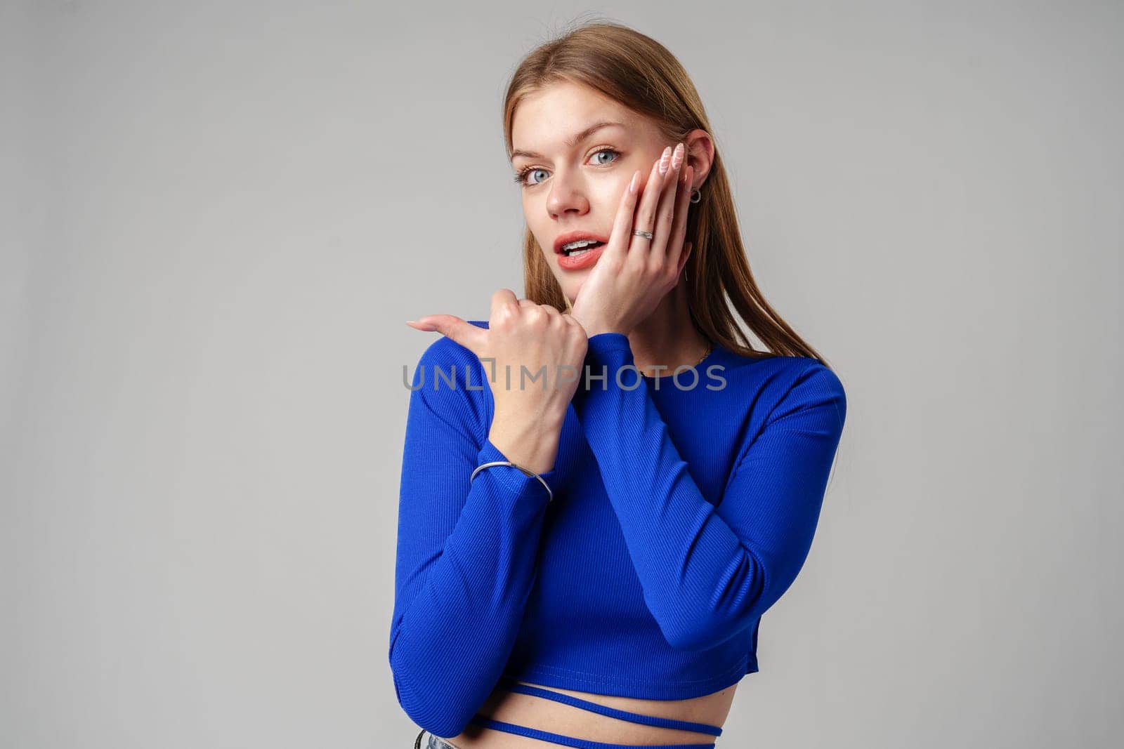 Woman in Blue Top Pointing With Hand Against Neutral Background in studio