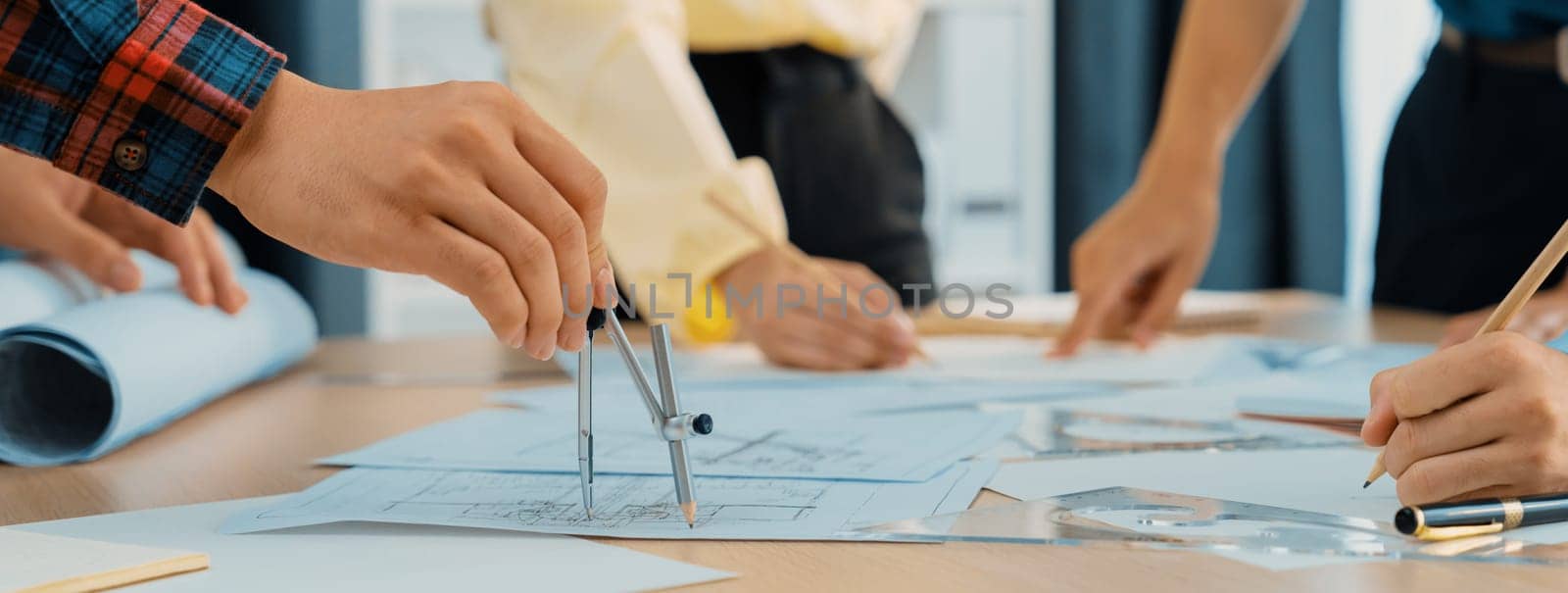 Skilled architect engineer team discuss about architectural project while project manager using laptop analysis data at meeting table with architectural document scatter around. Closeup. Delineation.