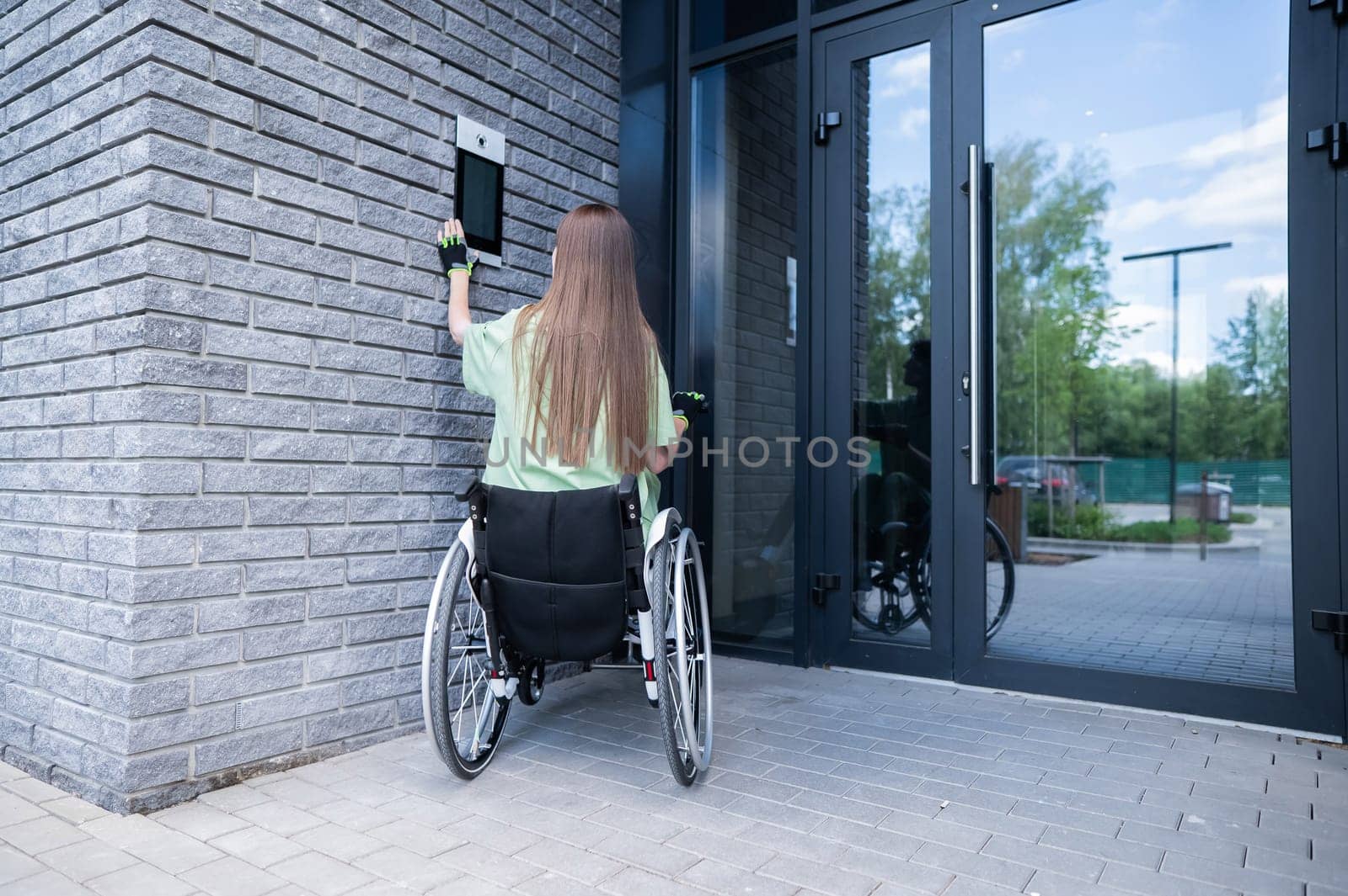 A woman in a wheelchair with an assistive device for manual control enters the entrance. Electric hand bike. by mrwed54