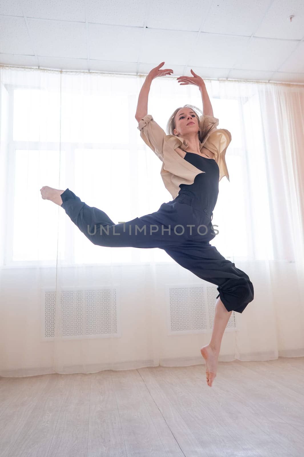 Caucasian woman dances contemporary in ballet class. Dancer in a jump. Vertical photo