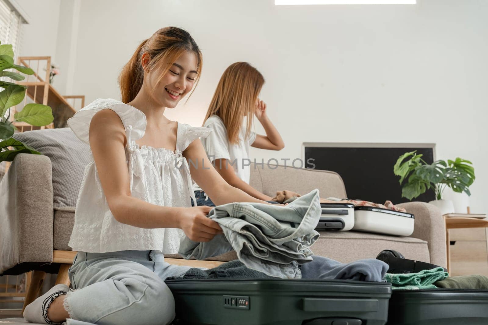 Two young female friends pack a suitcase with clothes and travel passports in preparation for a weekend away. by wichayada